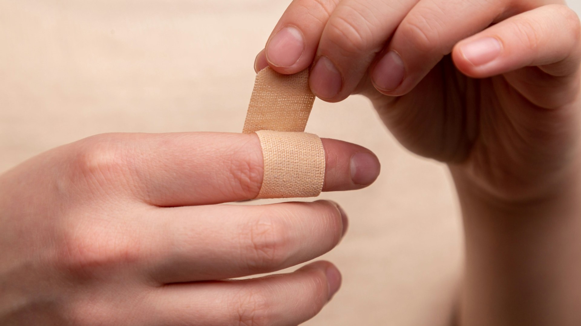 Een persoon plakt een pleister op een gewonde vinger, mogelijk na een klein bedrijfsongeval.