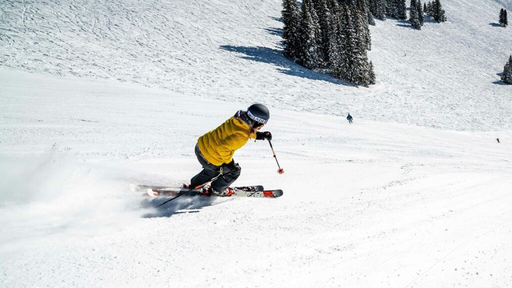 Skiër in gele jas maakt een bocht op een besneeuwde piste, ideaal voor wie wil skiën dichtbij huis