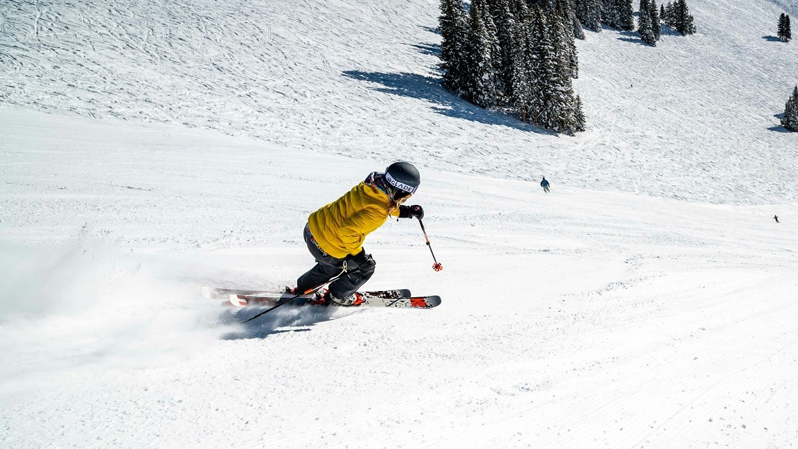Skiër in gele jas maakt een bocht op een besneeuwde piste, ideaal voor wie wil skiën dichtbij huis