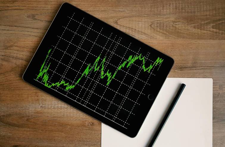 Tablet met groene koersgrafiek op houten tafel, symbool voor financieel advies of marktanalyse