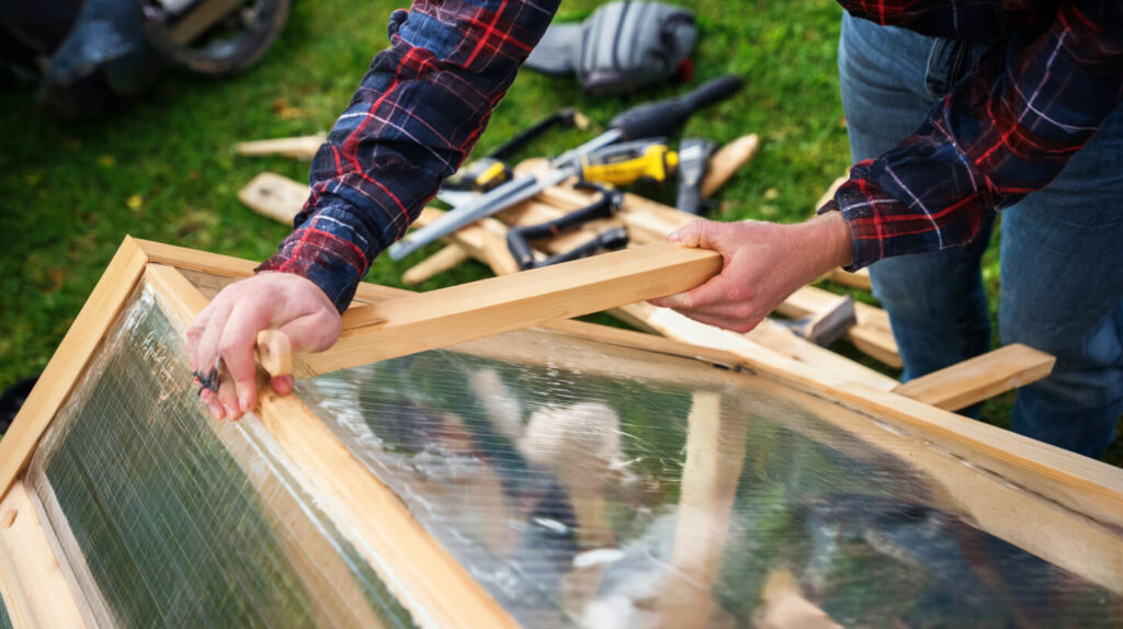 Bouw van een hobbykas tuin met houten frame en transparante panelen tijdens de montage.